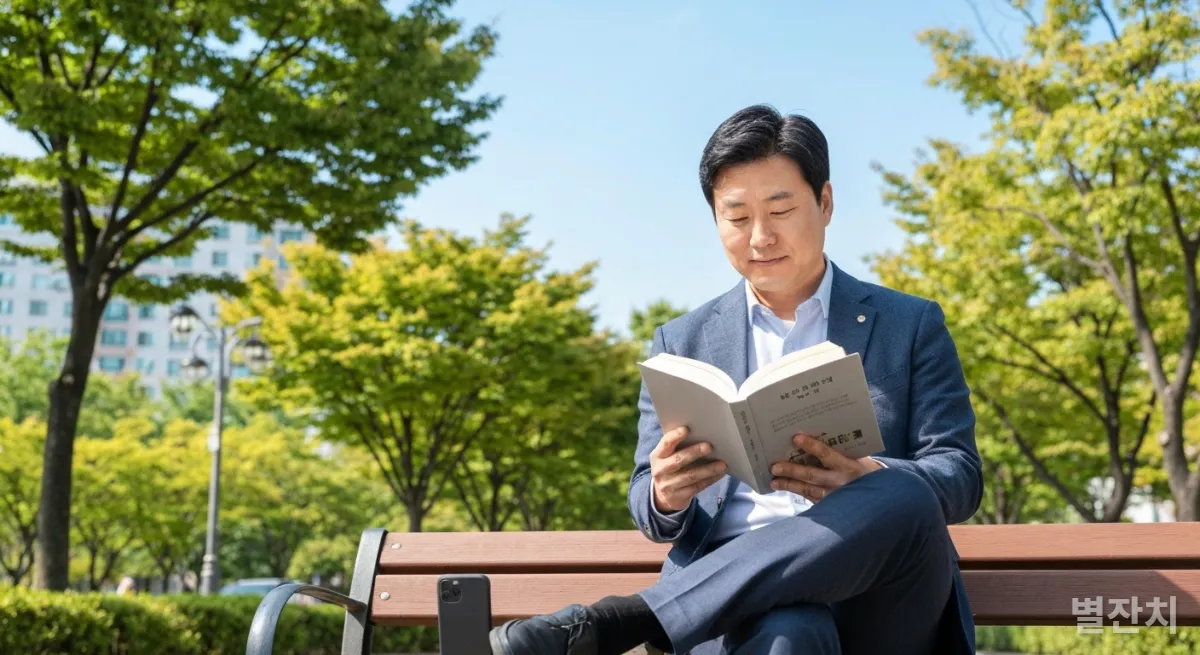 공원 벤치에 앉아 독서에 집중하는 한국인 남성, 스마트폰은 뒤집어 놓여있음