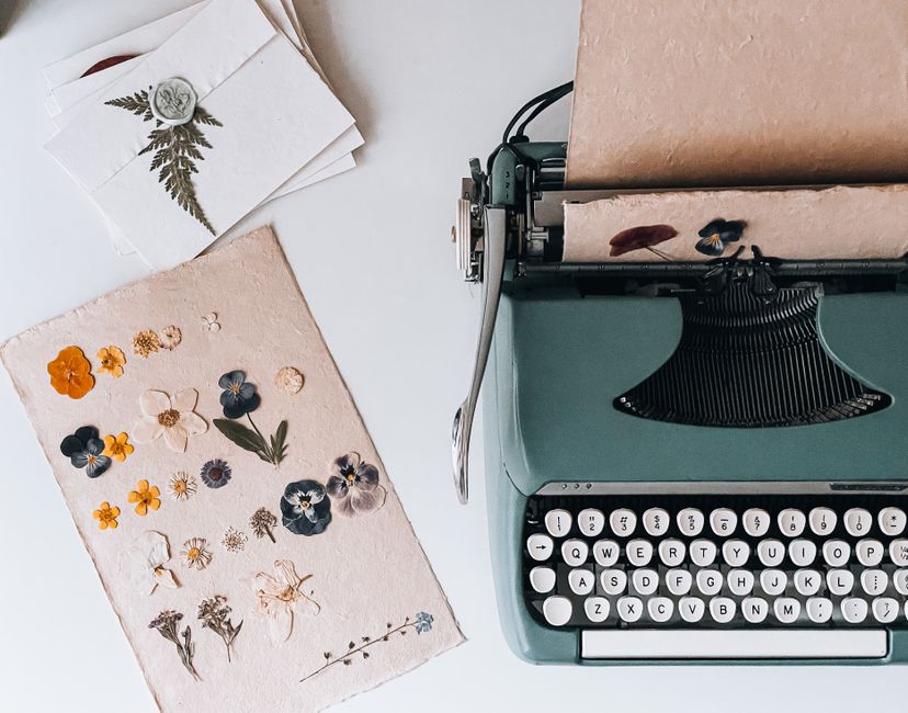 A vintage typewriter with dried flowers on paper and decorative cards arranged in a flat lay setting.