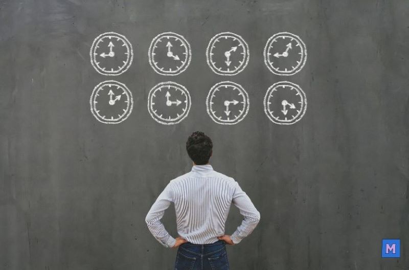 시간관리를 고민하는 비즈니스맨이 벽에 그려진 8개의 시계를 바라보며 서 있는 모습 via canva