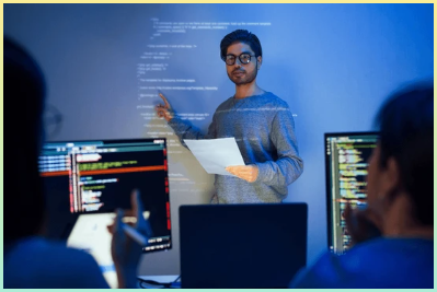 아시아 개발자는 소프트웨어 개발에서 동료들과 함께 팀워크와 지식 공유로 벽에 투영된 코드를 가리키며 현재 코드 검토 세션을 주도합니다.