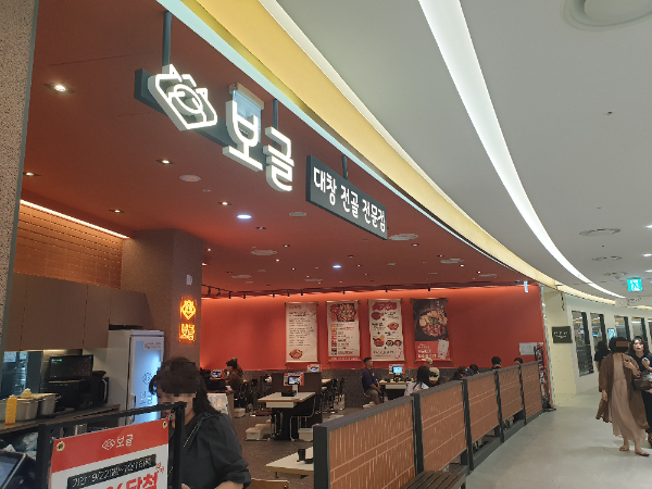 주황색 벽면에 보글 그리고 대창 전골 전문점이라는 간판이 보이는 식당. 카운터에서 계산하는 고객이 보인다.
