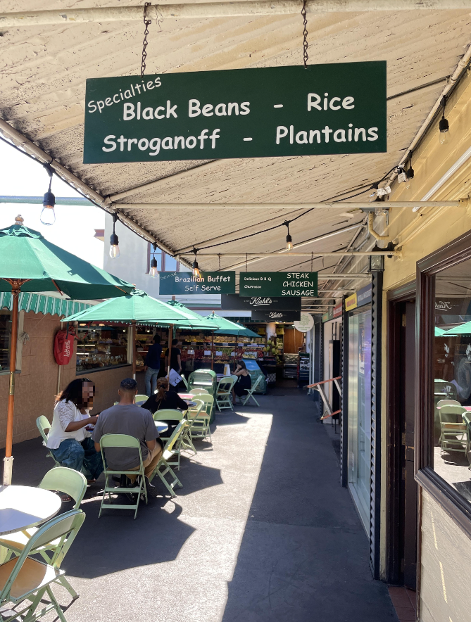 파머스 마켓 내부에 있는 팜파스 그릴 식당 앞의 모습. 위로는 여러 상점의 이름이 초록 간판 위에 하얀 글씨로 쓰여 있다. 왼쪽에는 초록 파라솔과 테이블&amp;#44; 의지가&amp;#44; 오른쪽에는 상점들이 있다. 