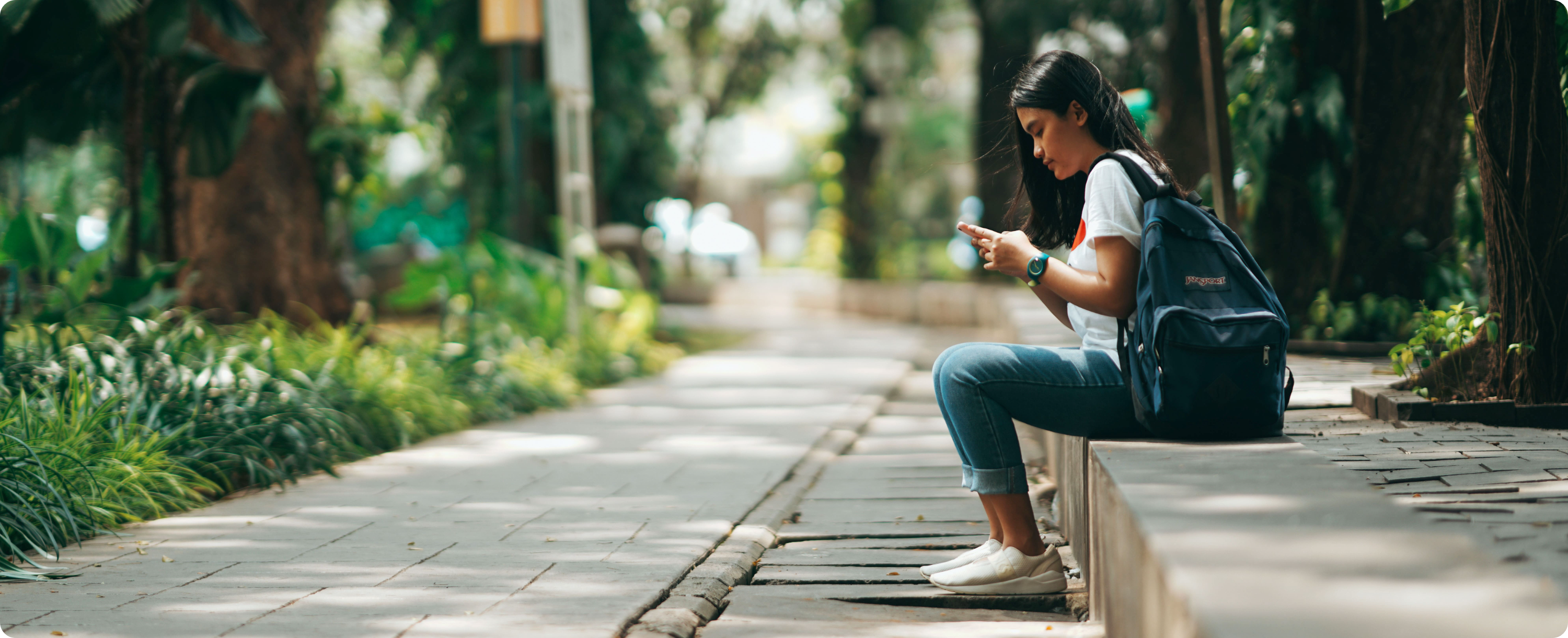 A person sitting on the side of the road and using a smartphone