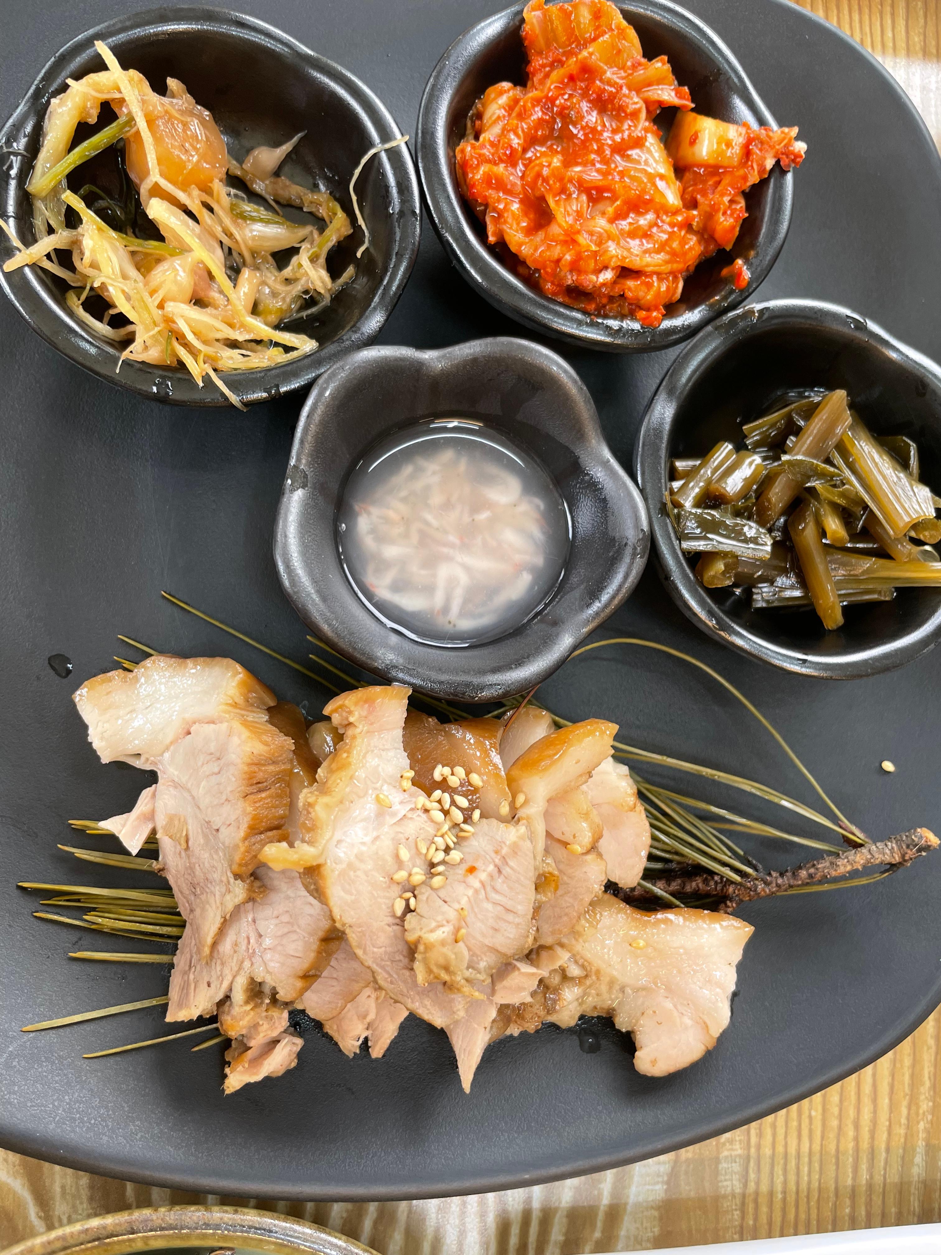 솔잎을 깐 접시에 약돌돼지와 새우젓, 달래장아찌, 곰취장아찌, 볶은 묵은지가 곁들임으로 나왔어요