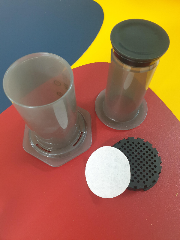 테이블 위에 에어로프레스가 놓여있다. 체임버, 플린저, 캡 그리고 필터로 결합해제 상태