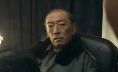 대머리에 군복을 입고 앉아 있는 영화 서울의 봄에서 배송학을 연기하는 염동헌