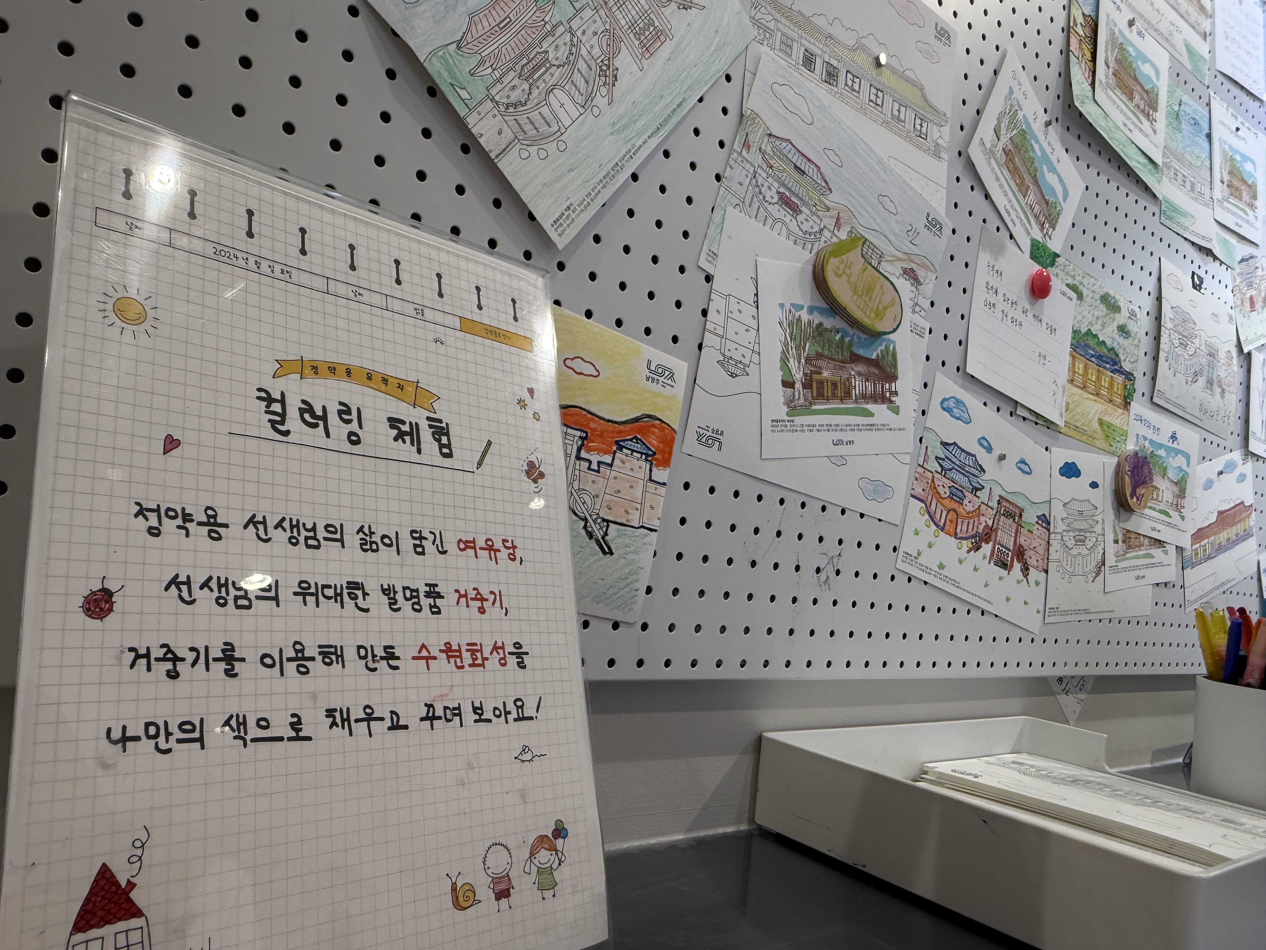 정약용 문화관의 컬러링 체험 안내문. 거중기를 그려보는 내용과 함께 아이들이 그린 그림들이 벽에 붙어 있다.