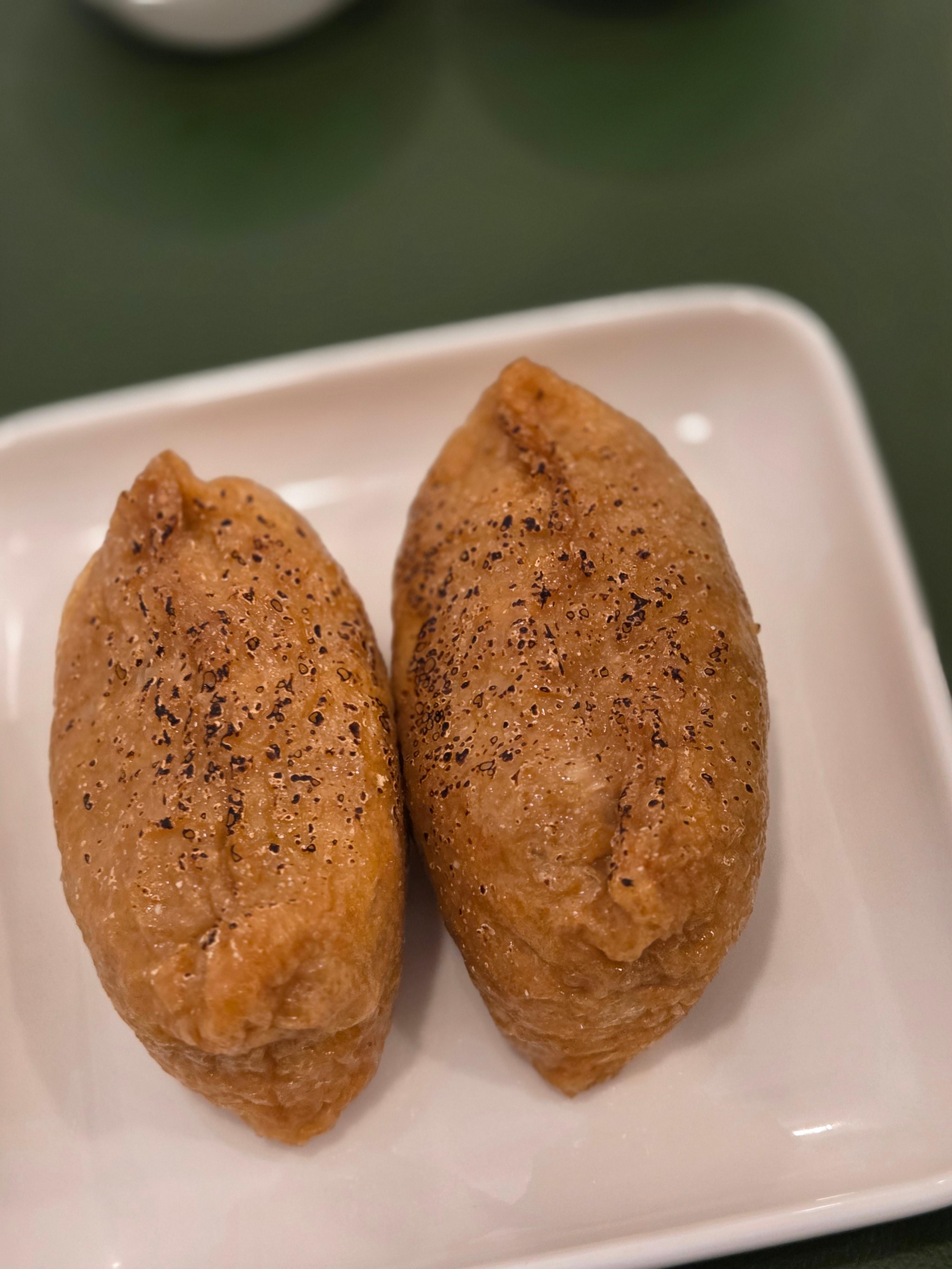 아부리된 유부로 감싼 유부초밥 두 개가 흰색 접시에 가지런히 놓인 모습.