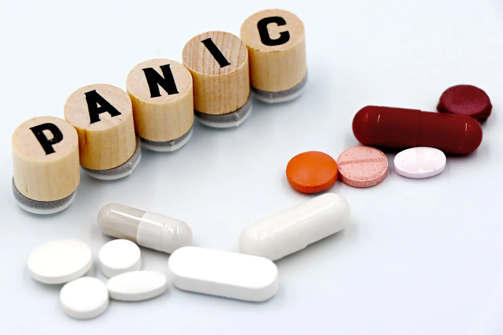 'PANIC'이라는 글자가 적힌 나무 타일 옆에 각종 알약이 배열되어 있는데, 이는 불안 치료를 상징합니다.