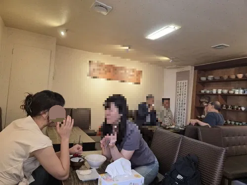 나무 테이블과 소파에 앉아 차를 마시는 손님들, 벽면 찻잔 진열장이 보이는 귀천 실내