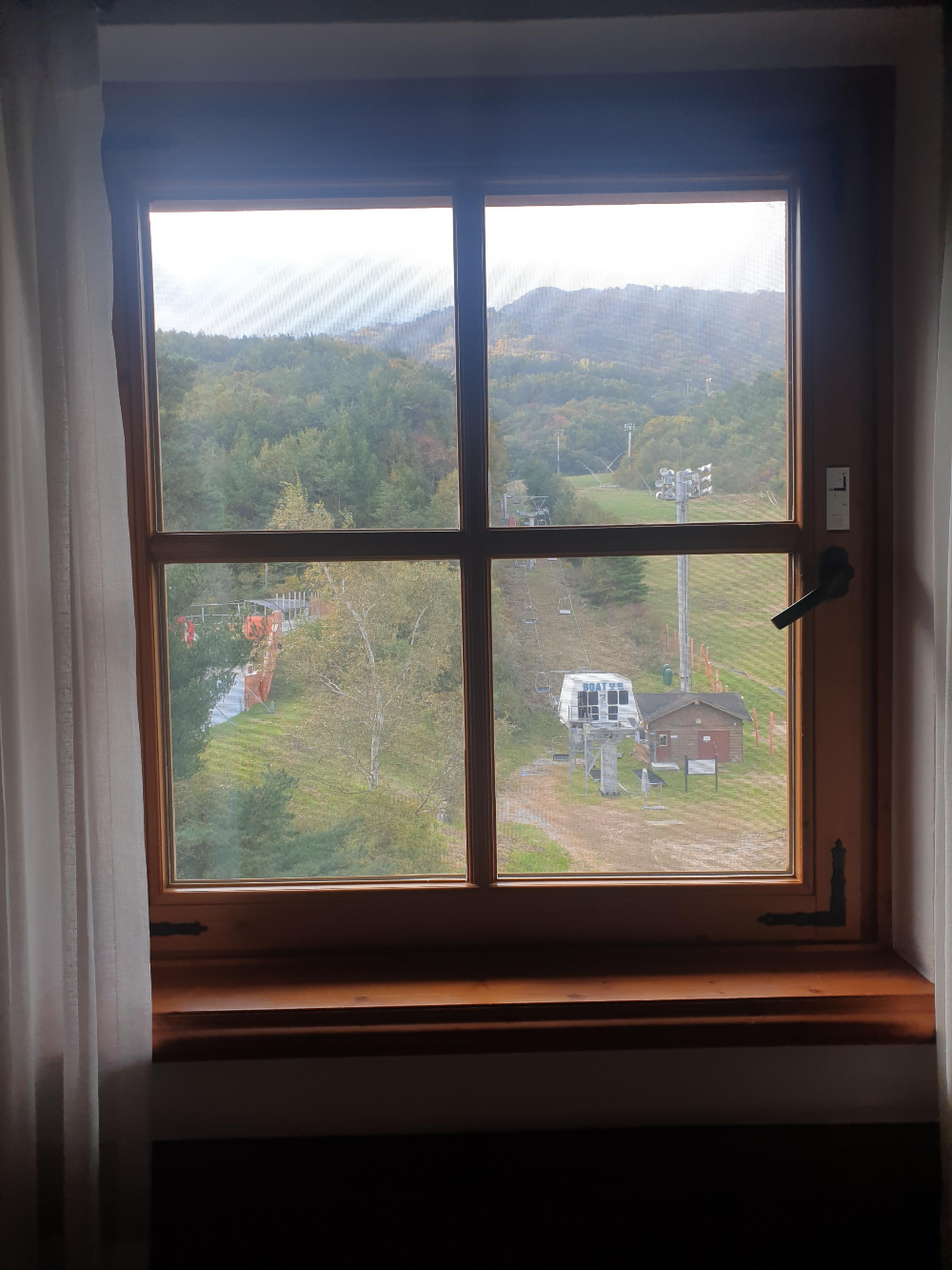 창 밖으로 산이 보인다. 산 에는 스키장 슬로프와 리프트 장치가 보인다.
