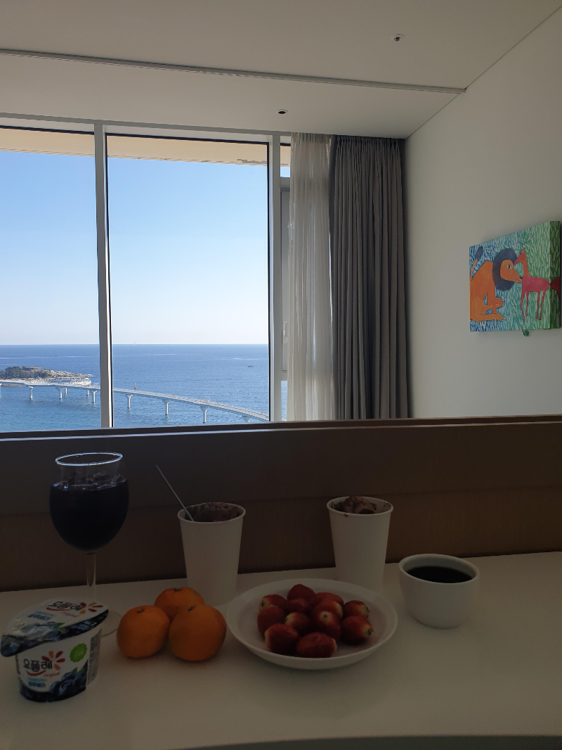 창 밖으로 바다가 보이고 내부에는 바 테이블이 있다. 바 테이블에는 과일과 커피가 세팅 되어 있다.