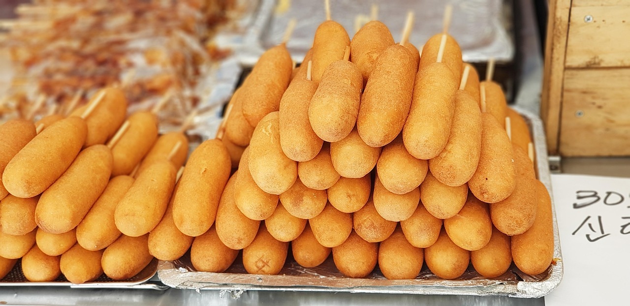A stack of freshly fried Korean corn dogs (hot dogs) on skewers, displayed at a Seoul street food stall.