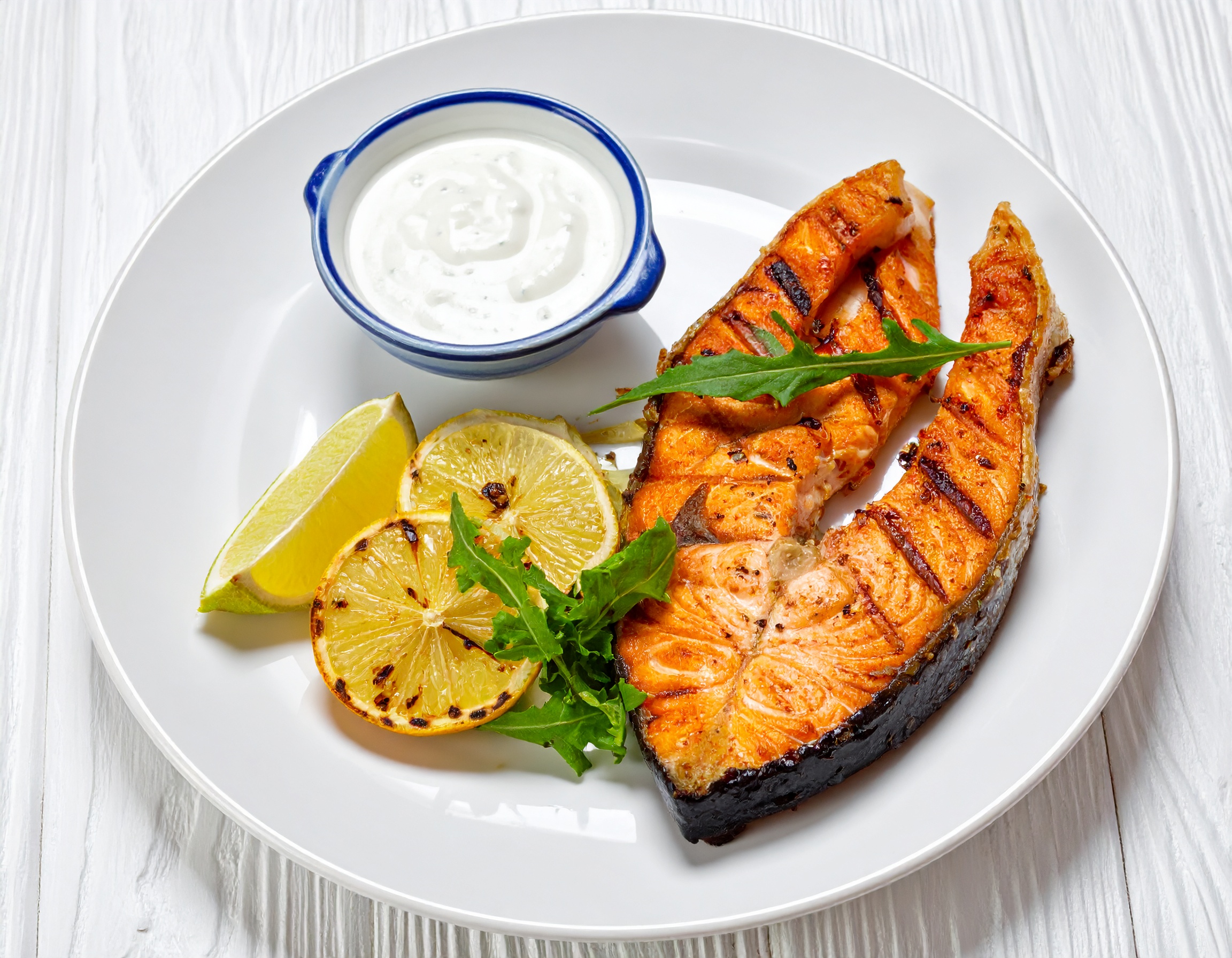 그릴에 구운 연어와 구운 레몬, 요거트 소스가 함께 제공된 건강한 단백질 식단