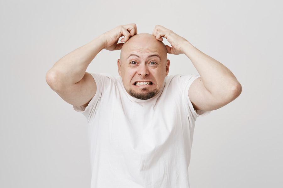 머리를 밀어버린 서양 남성이 양쪽 손을 머리에 대고 끓어오르는 화를 주체하지 못하고 분노를 표출하고 있는 것을 찍은 사진