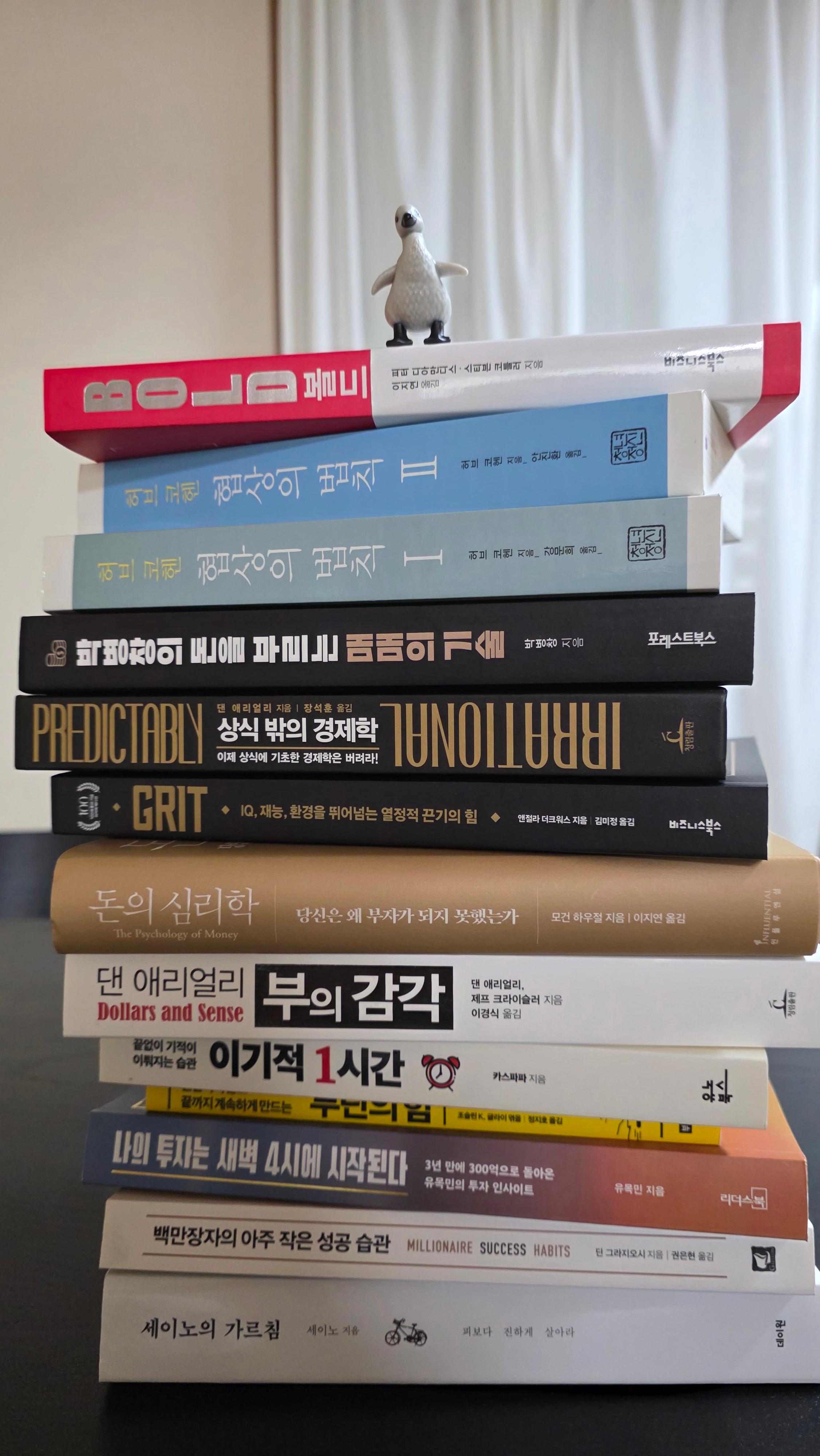 12권의 책이 쌓인 북타워 꼭대기에 서 있는 펭귄 피규어