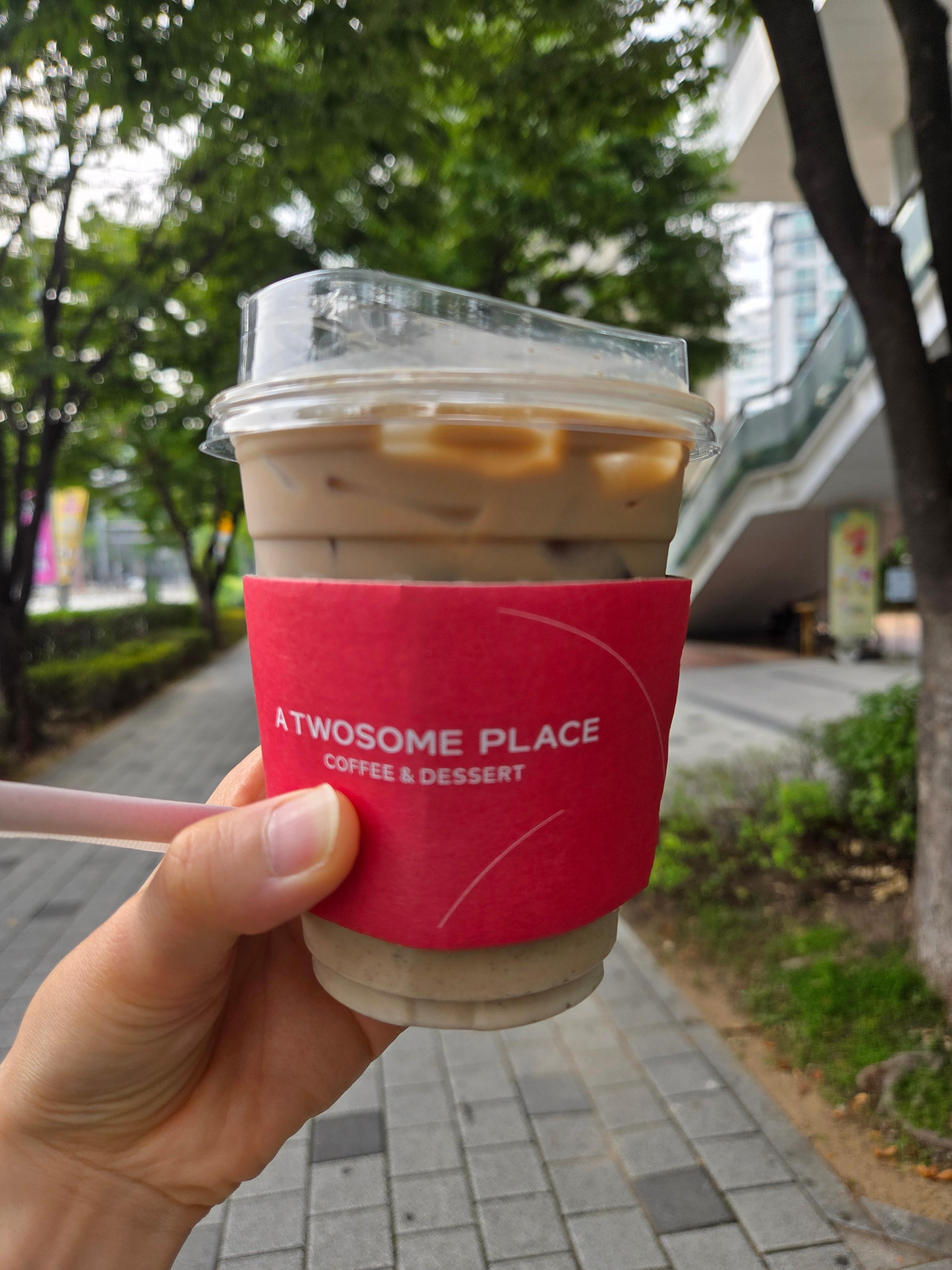 투썸플레이스 바닐라빈 콜드브루 라떼를 빨간 컵홀더에 담아 야외에서 들고 있는 모습