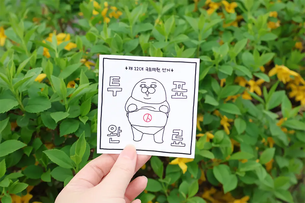 초록잎과-개나리-배경으로-투표-인증-종이-들고-있는-손
