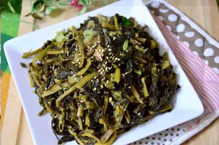 흰 사각 접시에 담긴 시래기나물 무침 요리로, 잘게 썬 시래기에 참깨가 고루 뿌려져 있으며 자연스러운 갈색과 초록빛이 어우러진 전통 한식 반찬.