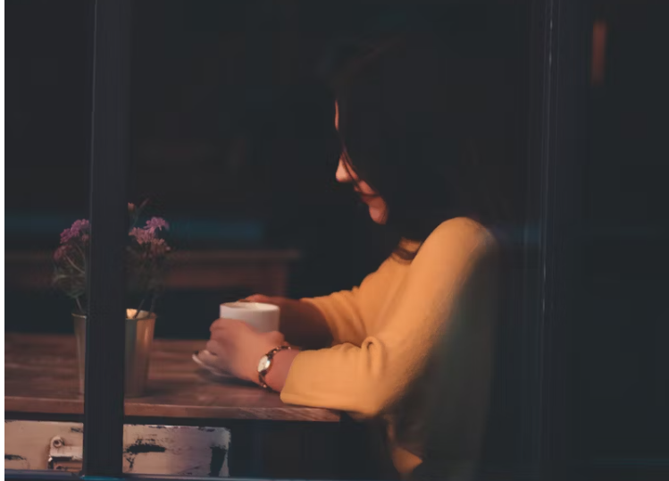 따뜻한 조명 아래 앉아 커피를 마시며 생각에 잠긴 여성의 모습