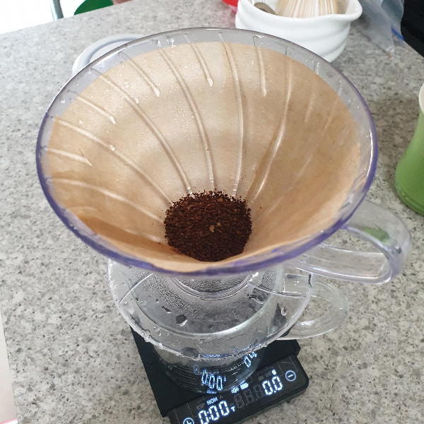 저울위에 유리 서버, 서버 위에 드리퍼가 있다. 드리퍼 안쪽에 분쇄된 원두 가루가 있다.