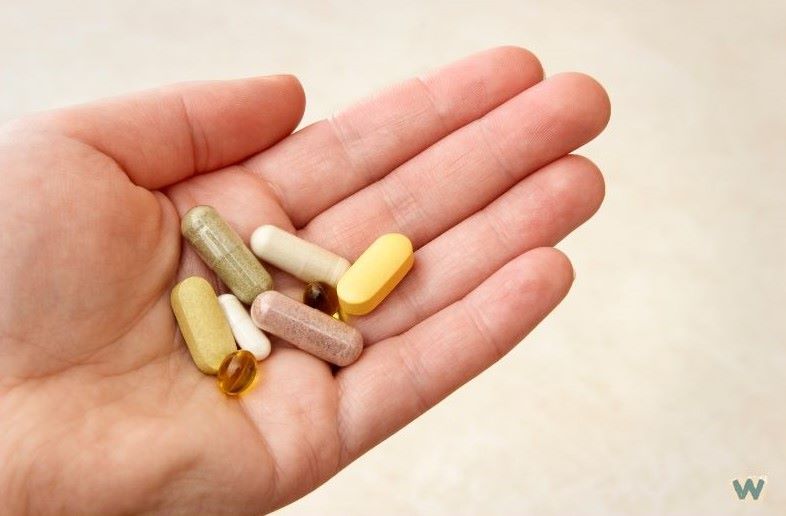 손바닥 위에 놓인 다양한 색깔의 비타민 알약들 - 노란색, 흰색, 갈색 캡슐과 정제 비타민 보충제 via Canva