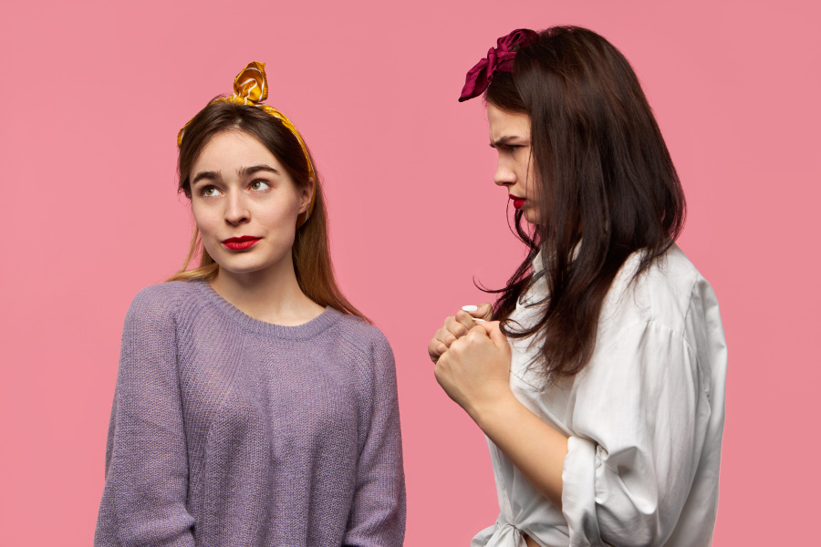 보라색 상의를 입고 머리에 금색 때를 맨 젊은 여성이 오른쪽 위를 보고 있고, 그 옆에 흰색 셔츠를 입은 여성이 질투가 나서 화가 난 표정으로 쳐다보고 있는 것을 찍은 사진