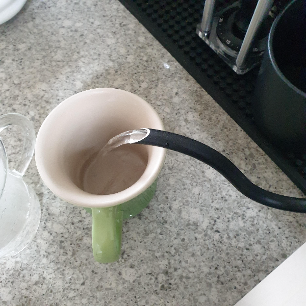 초록색 컵에 드립포트로 뜨거운 물을 붓고 있다. 예열 과정