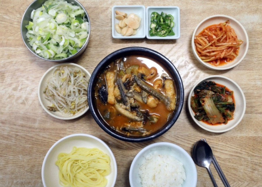 야생에서 채취를 한 미꾸라지를 넣고 끓인 도랑탕을 테이블 중앙에 놓아두고 김치와 파, 무생채, 숙주나물, 소면, 밥, 마늘, 고추, 김치, 숟가락, 젓가락을 그 옆에 놓아두고 찍은 사진