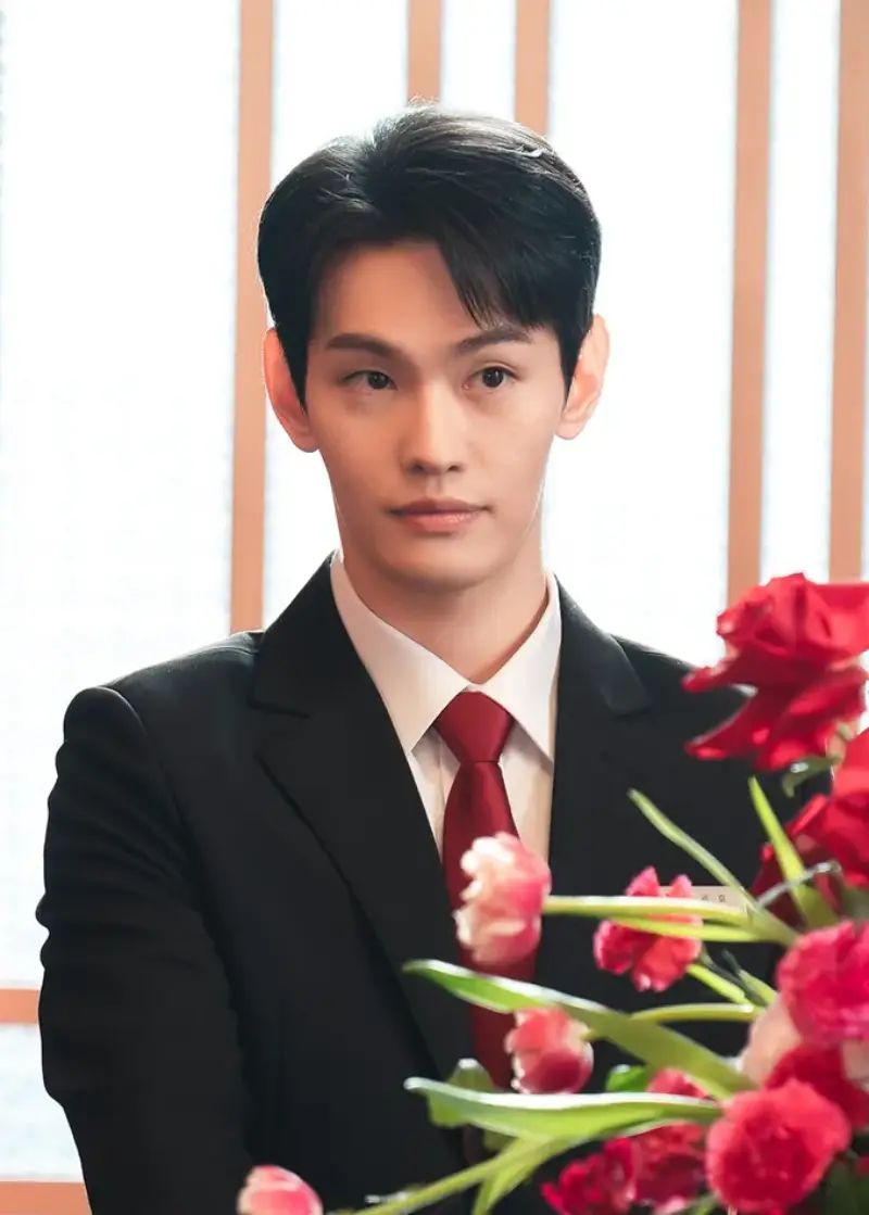 호텔을 배경으로 검은색 정장의 사원복을 입고 누군가를 응시하고 있는 세호