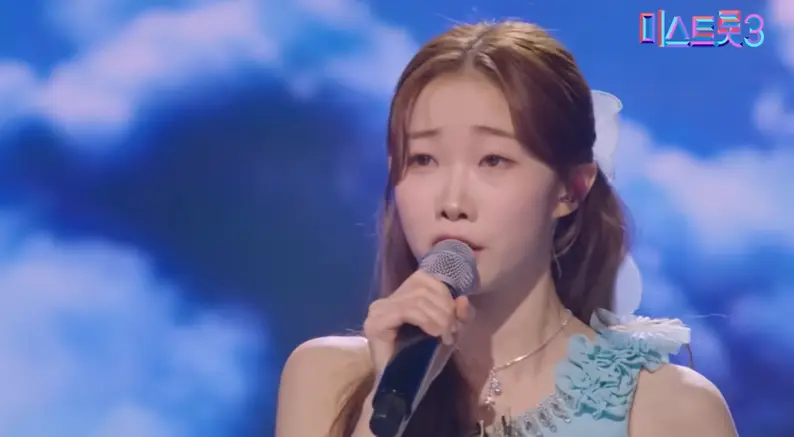 미스트롯3- 파란배경 파란드레스를 입고 오른손으로 마이크를 들고 긴머리를 늘어뜨리며 노래하는 정서주