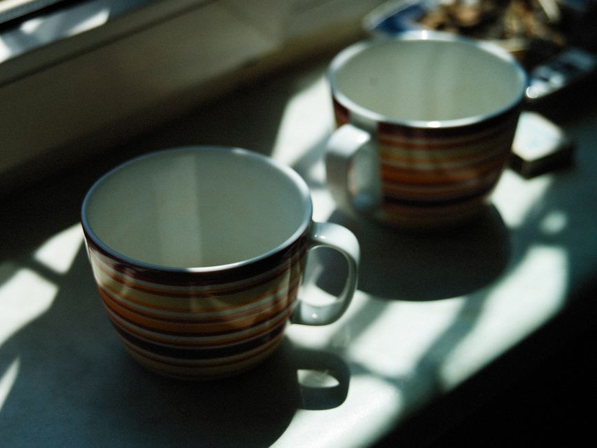 Two sunlit striped cups on a kitchen windowsill create a cozy atmosphere.