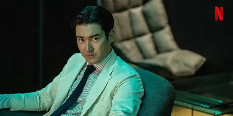 편하게 보이는 쇼파에 등을 댄 채 흰색 양복을 입고 앉아 누군가를 노려보고 있는 홍 이사