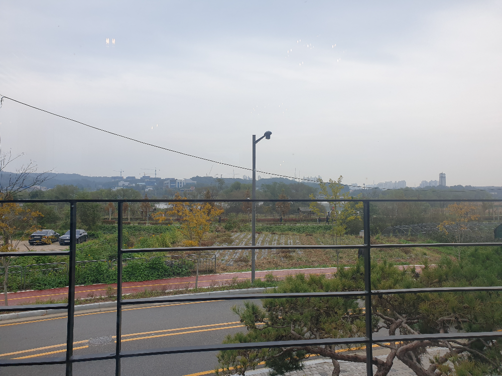 창문 너머 금속 테라스 철제 낙상 방지 구조물과 그 뒤로 보이는 논과 나무들