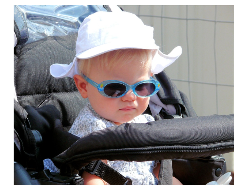 "선글라스와 모자를 쓴 아기가 유모차에 앉아 있는 모습, 아기 안전을 위한 유모차와 카시트 선택의 중요성을 상징하는 장면"