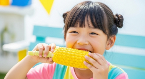 초당옥수수를 한입 베어 먹은 후 환하게 웃는 한국 아이의 모습&amp;#44; 밝은 배경