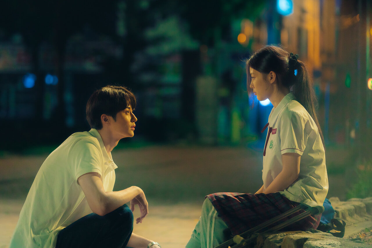 20세기 소녀 영화의 한장면. 어두운 밤 공원 가로등 조명 아래 남자 주인공과 여자 주인공이 앉아서 서로를 바라보고 있다.
