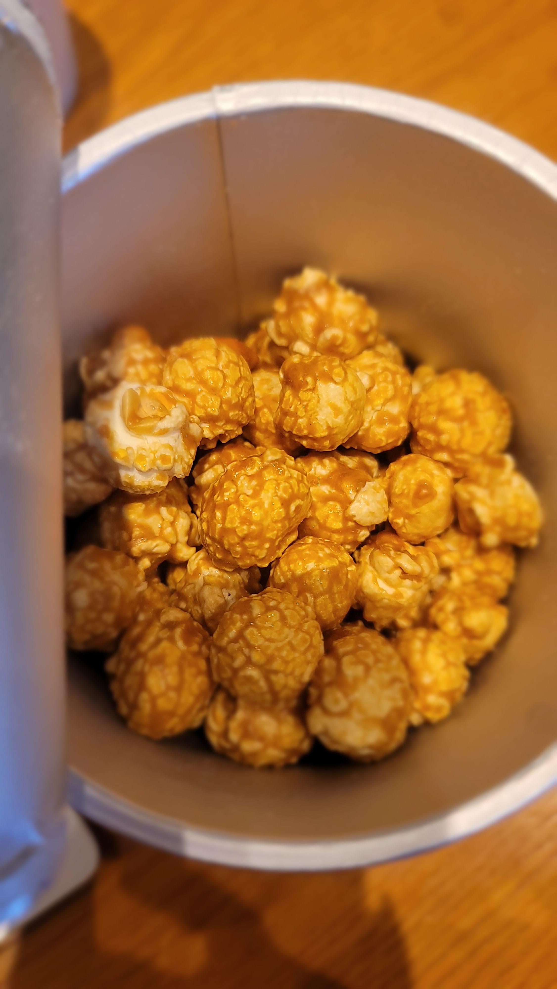 용기 안에 담긴 카라멜 코팅 팝콘의 근접 사진, 둥글고 윤기 나는 갈색빛을 띄는 팝콘이 보임