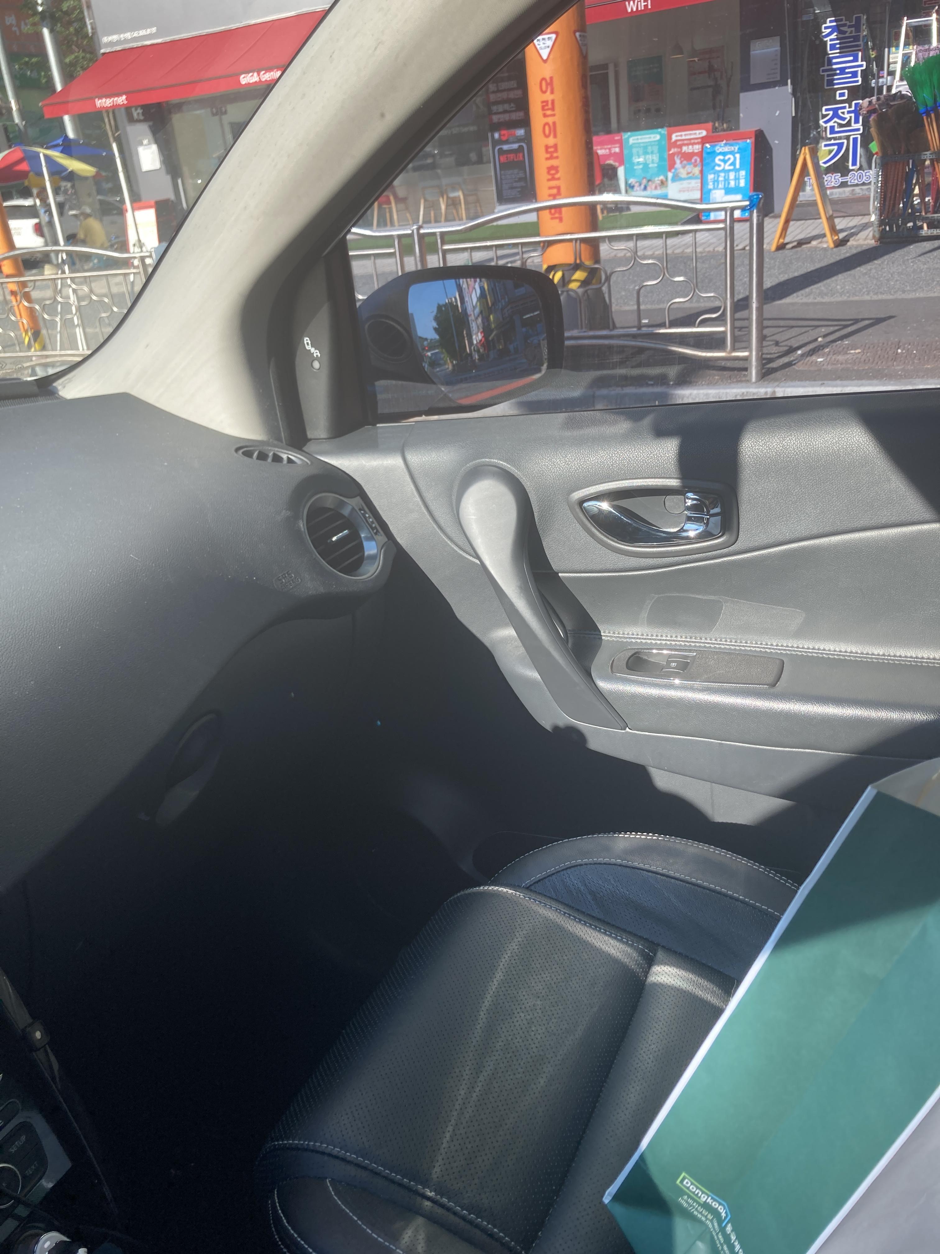 햇빛이 강하게 들어오는 차량 조수석 창가, 검은 가죽 시트와 사이드미러가 보임