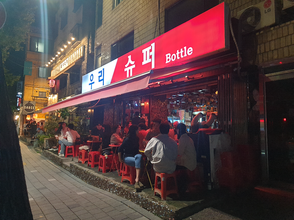 어두워진 저녁에도 야외 좌석은 손님들로 가득하다. 우리슈퍼 간판 조명이 들어와 있다.
