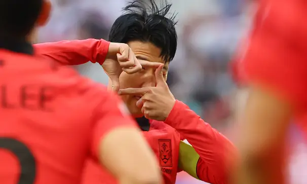 사우디전- 붉은긴팔유니폼 오른팔에 노란완장을 차고 두손으로 카메라 세러머니를 하고있는 손흥민