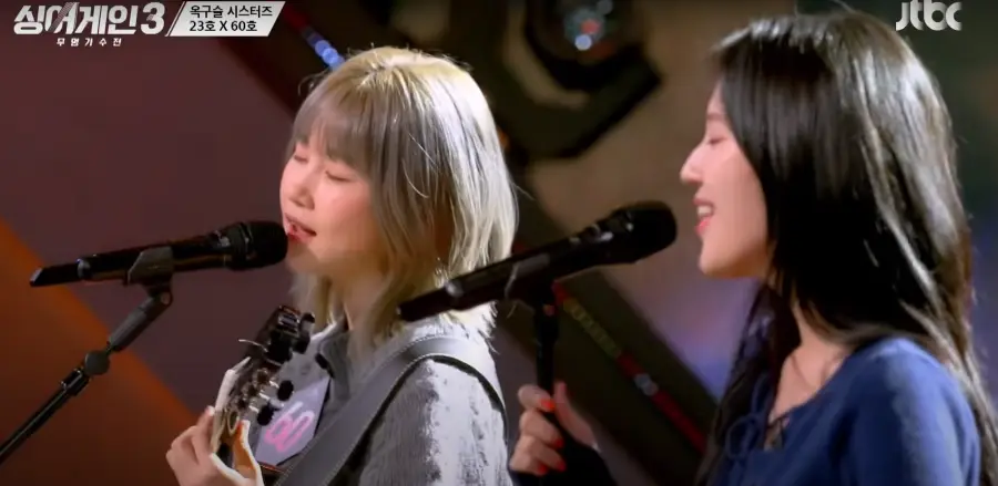 싱어게인 3- 단발머리를 늘어뜨린채 눈감고 기타를 치며 노래하는 60호와 웃으며 노래하는 23호 상반신