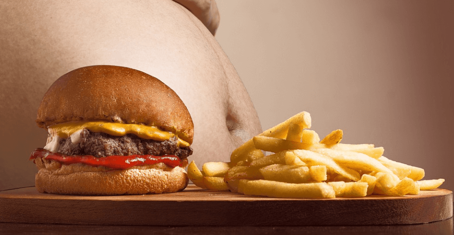 비만이 남자 배 앞에 햄버거와 감자 튀김이 놓여 있다