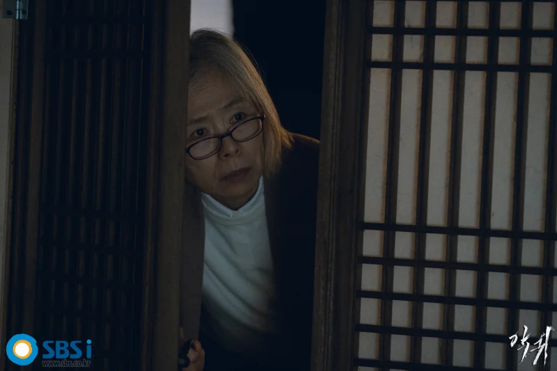 전통 문살과 한지로 바른 방문을 반쯤 열고 어딘가를 응시하면서 안경을 쓰고 있는 김석란