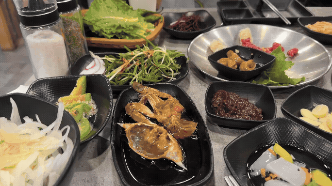 삼거리 명품한우 밑반찬 상차림. 상추, 파채, 양파, 장아찌, 육회, 간장게장, 된장무침 등 다양한 한식 반찬이 가지런히 차려져 있다.