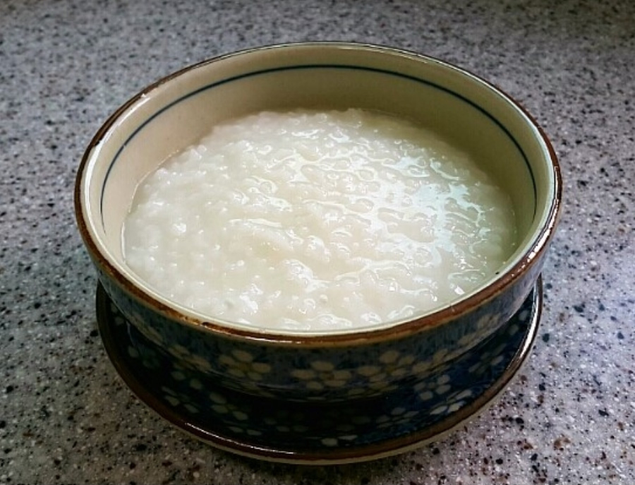 하얀 쌀을 끓여서 만든 쌀죽을 담은 동그란 그릇을 바닥 위에 그릇 받침대를 놓고 그 위에 놓아두고 찍은 사진