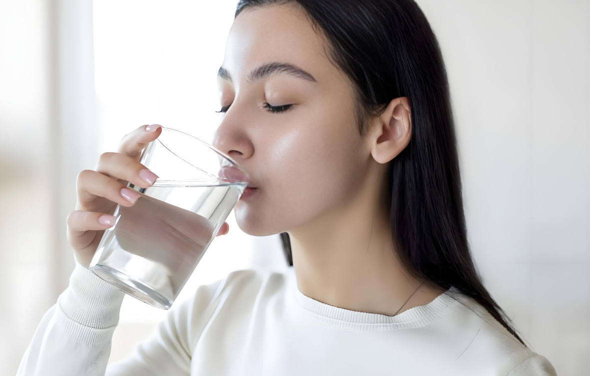 머리긴여성이투명유리컵에담기물을마시는모습
