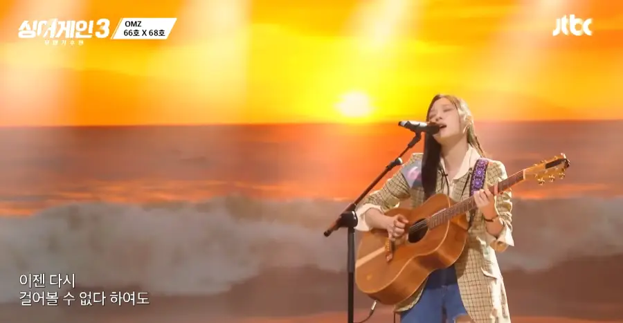 싱어게인3- 노란색 자켓을 입고 긴생머리를 늘어뜨린채 갈색 기타를 치며 스탠딩마이크앞에서 진지하게 노래하는 66호