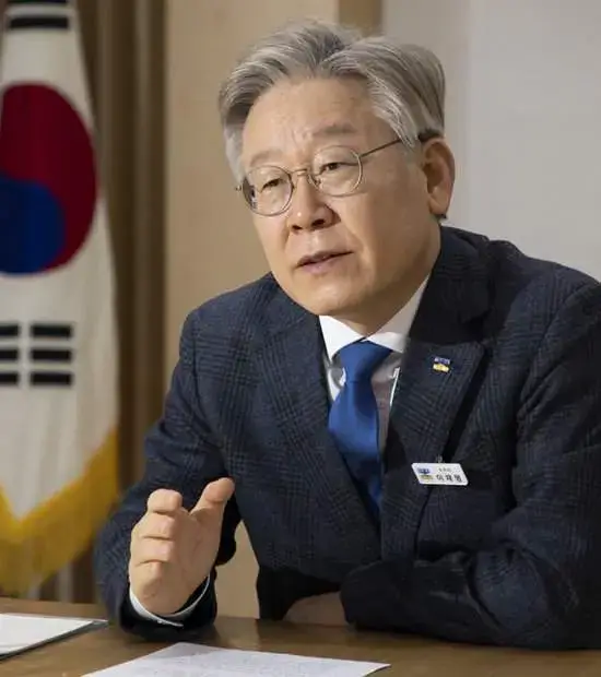 태극기를 배경으로 정책을 설명 중인 이재명 후보. 진지한 분위기에서 경제와 민생 비전을 언급.