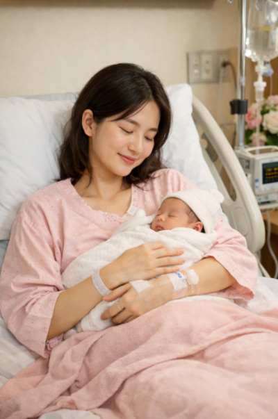 출산 직후 병원 침대에서 신생아를 안고 미소 짓는 산모의 모습, 산후 회복과 모성애를 상징